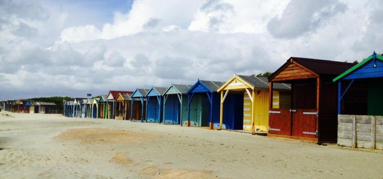 Row of colourful beach huts on a sandy shore, symbolising cultural diversity, individuality, and coexistence — key themes in transcultural therapy.