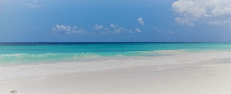 Tranquil beach with clear turquoise water and blue sky, symbolising presence, inner calm, and the spacious awareness cultivated through mindfulness.