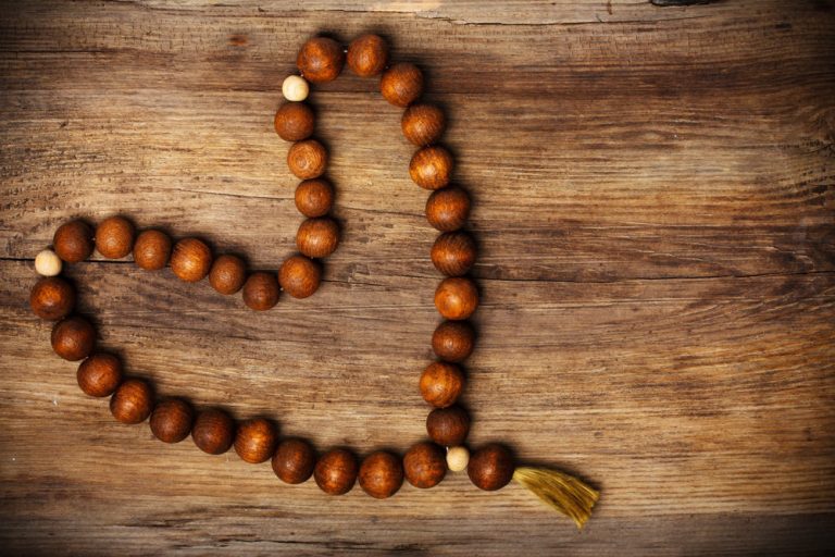 Wooden prayer beads shaped into a heart on a rustic wooden surface, symbolising spiritual connection, mindfulness, and embodied compassion.